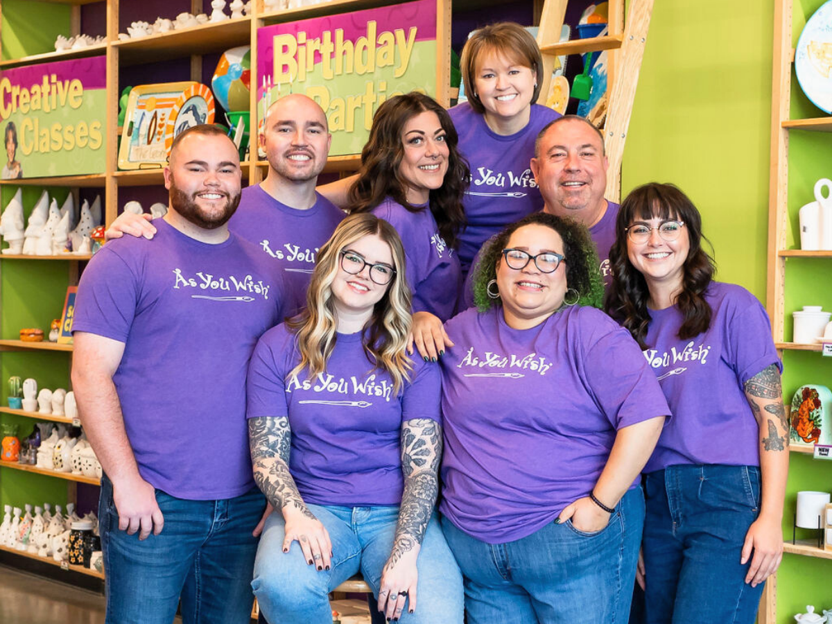 Group of people wearing purple 'As You Wish' shirts in a store setting.